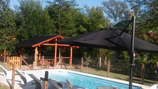 A backyard with a swimming pool, lounge chairs, and a covered seating area.
