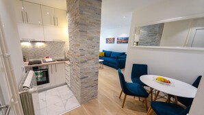Una cocina moderna con armarios blancos, una pared de acento de piedra y un comedor con sillas azules y una mesa blanca.