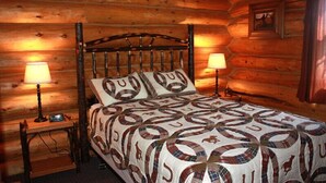 A log cabin bedroom with a wooden bed, two bedside lamps, and a quilt with circular patterns. - Rand Creek Ranch (Cody)