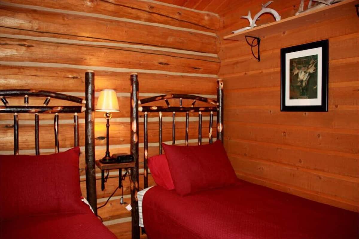 A wooden cabin room with two beds, a lamp, and a framed picture on the wall.