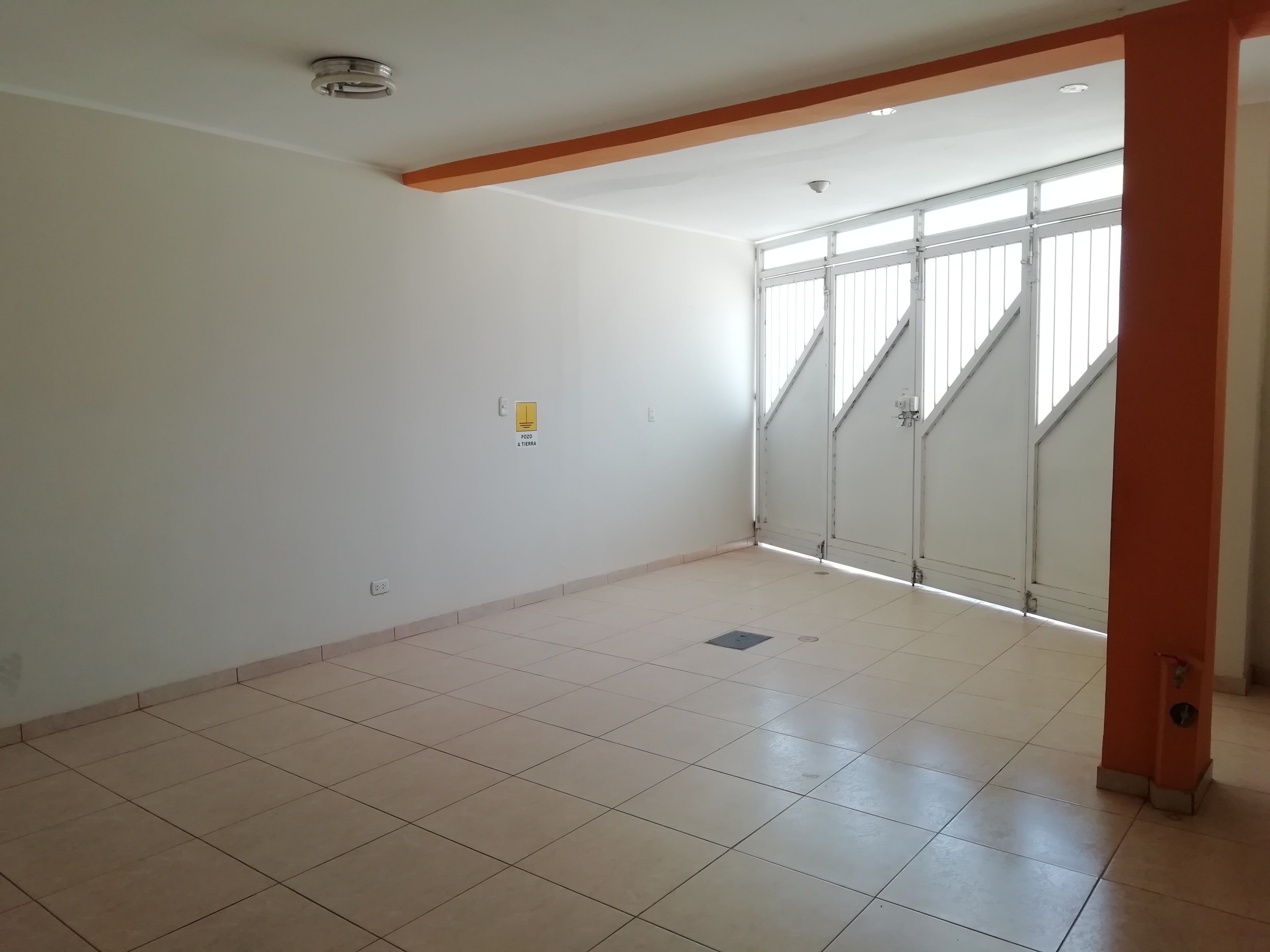 A spacious room with a tiled floor, a ceiling light, a door with a metal handle, and a window with a view of the outside.