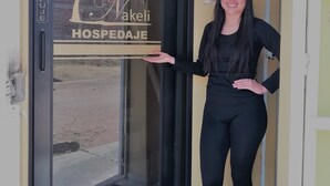 Una persona de pie frente a la entrada de un hotel, con un escaparate de vidrio que muestra el nombre "C. Wakeli HOSPEDAJE".