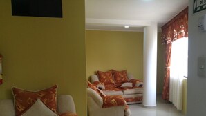 Un salón con dos sofás y una mesa de centro, paredes amarillas y una ventana con cortinas.