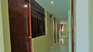 Un pasillo con puertas de madera, suelo de baldosas y una cortina roja al fondo.