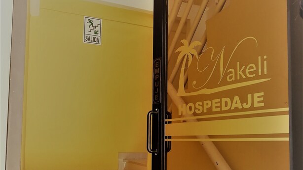 Entrada de hotel con puerta de vidrio que muestra el nombre 'Nakeli' y 'HOSPEDAJE'.