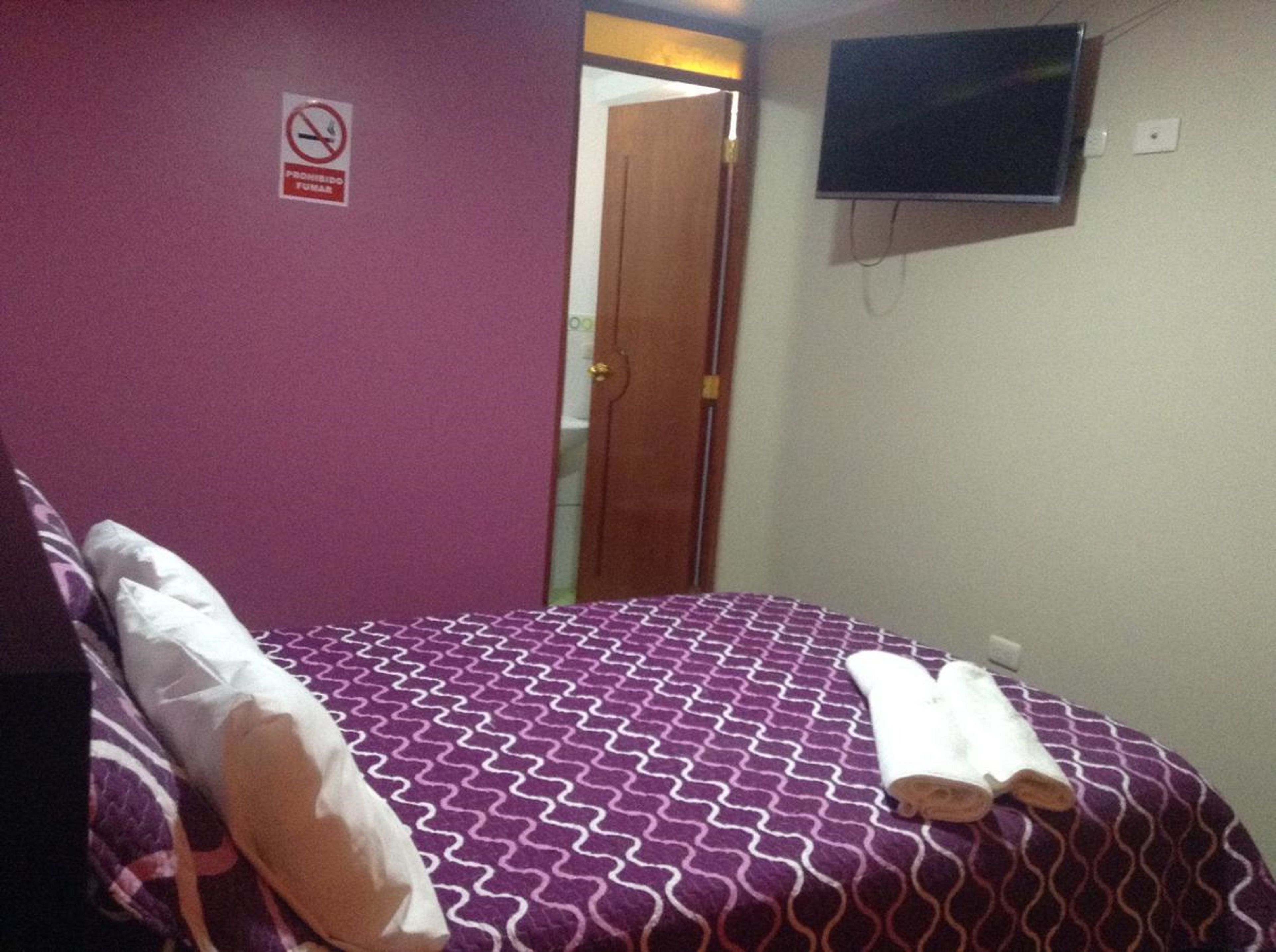 A hotel room with a bed, a television mounted on the wall, and a door leading to another room.