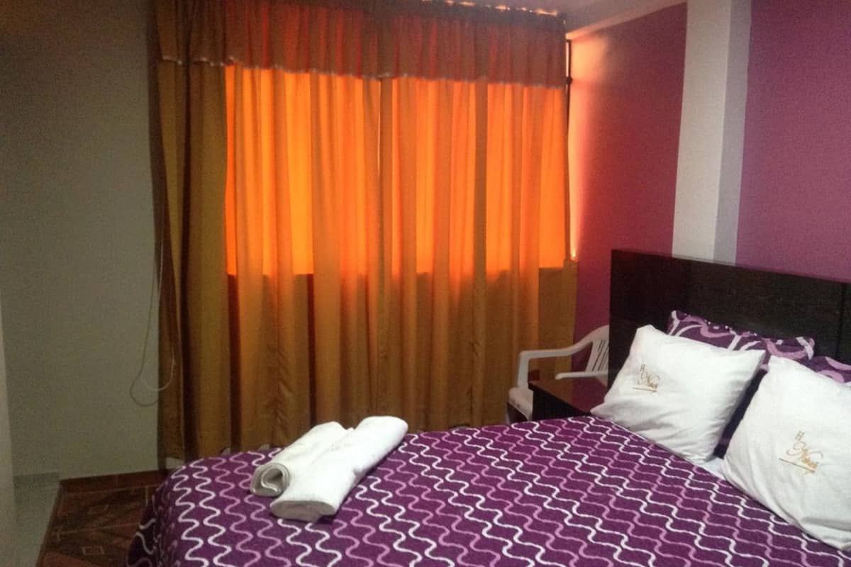 Quarto de hotel com uma cama, uma cadeira e uma janela com cortinas.
