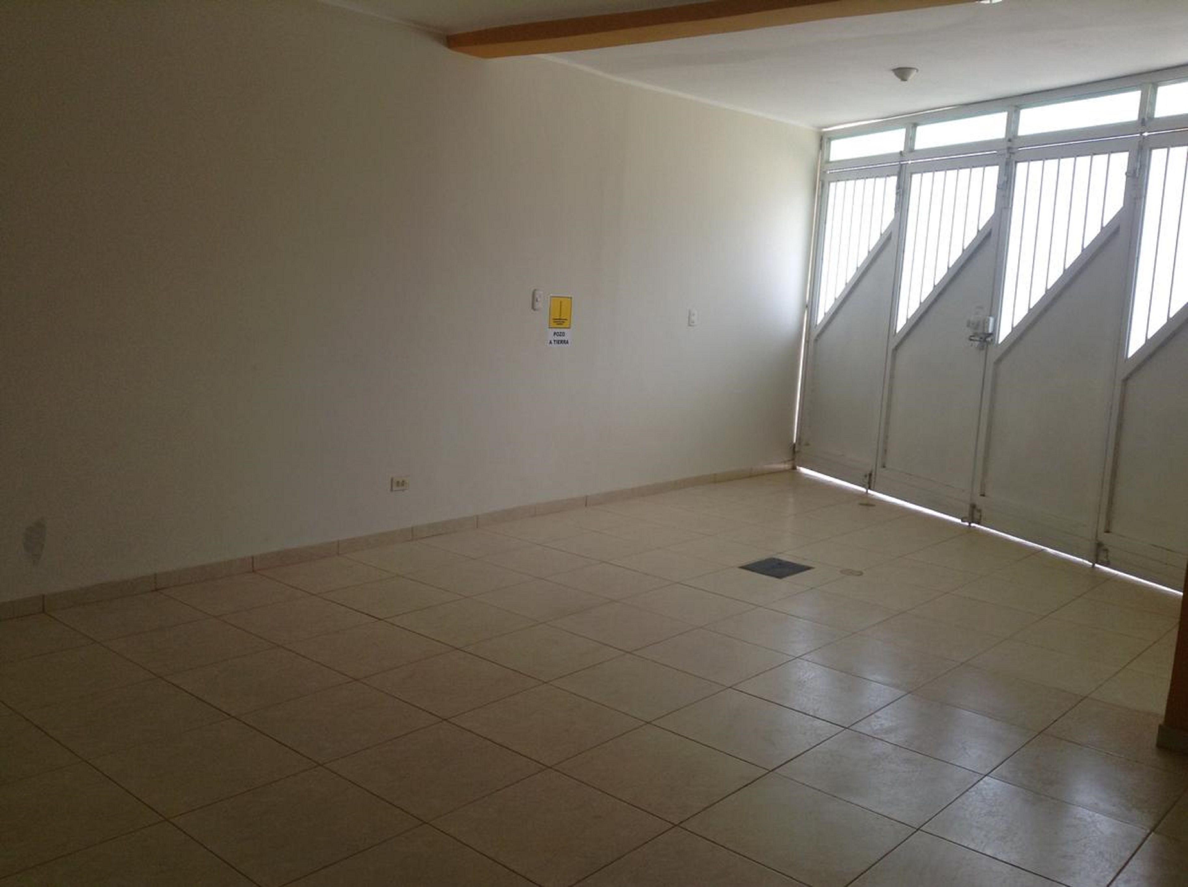 Una habitación vacía con piso de baldosas, un enchufe a la vista y una ventana con vistas.