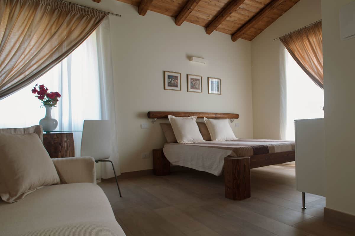Un dormitorio con cama de madera, un sofá y una silla. Hay tres cuadros en la pared.