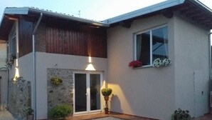Une maison à deux étages avec une façade en pierre, un étage supérieur en bois et un petit jardin agrémenté de plantes en pot.