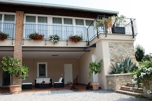 Un bâtiment à deux étages doté d’un balcon, de plantes en pot et d’un espace extérieur aménagé pour s’asseoir.