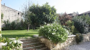 Un jardin avec un escalier en pierre menant à une maison, entouré de différentes plantes et bordé d’un chemin de gravier.