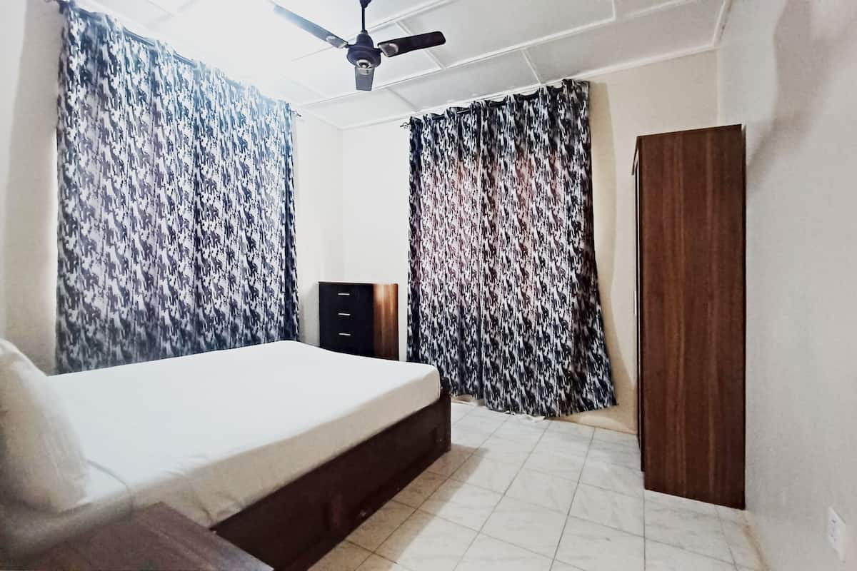 Un dormitorio con cama, armario, ventilador de techo y cortinas estampadas.