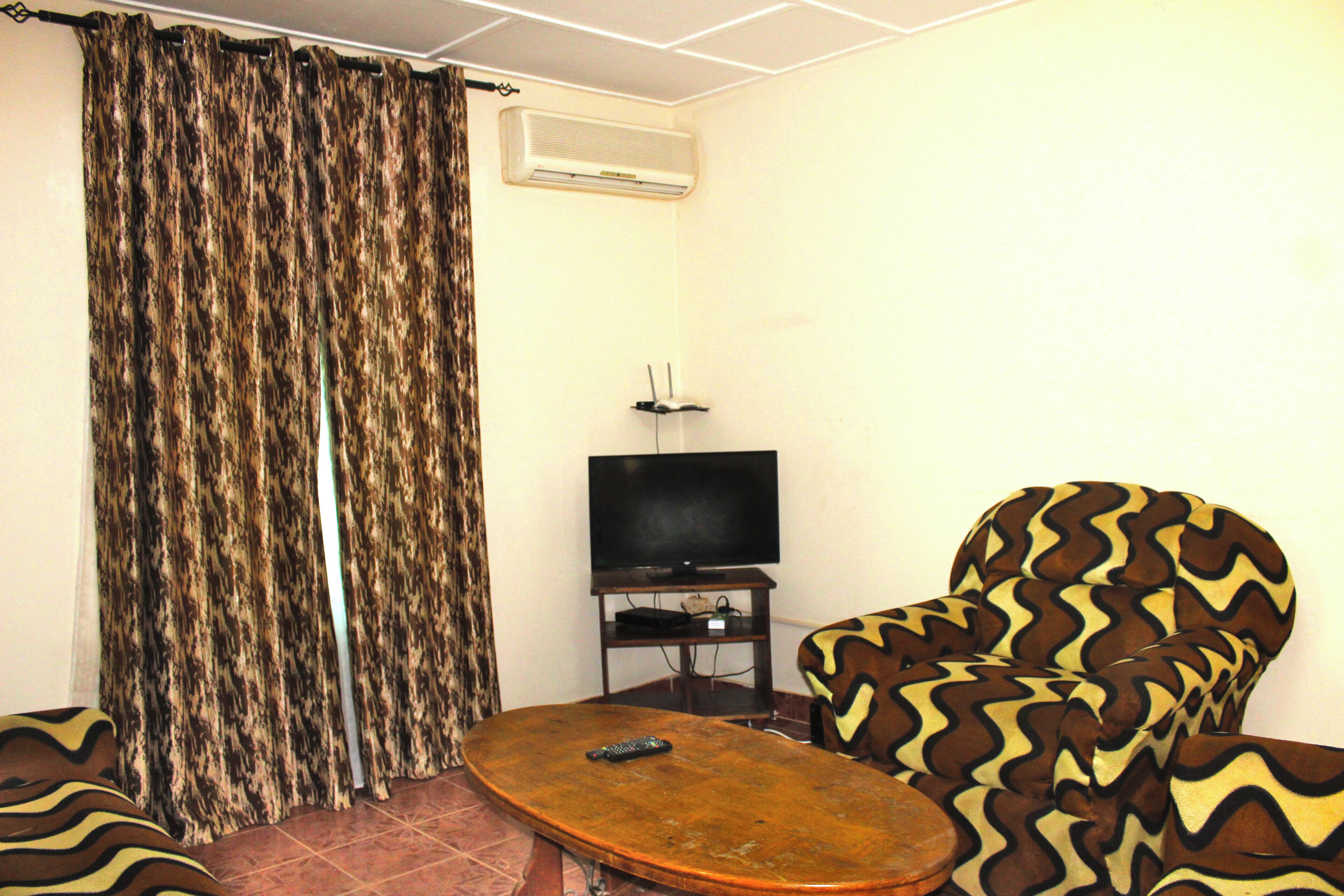 Una sala de estar con un sofá estampado, un televisor sobre un mueble bajo y una cortina.