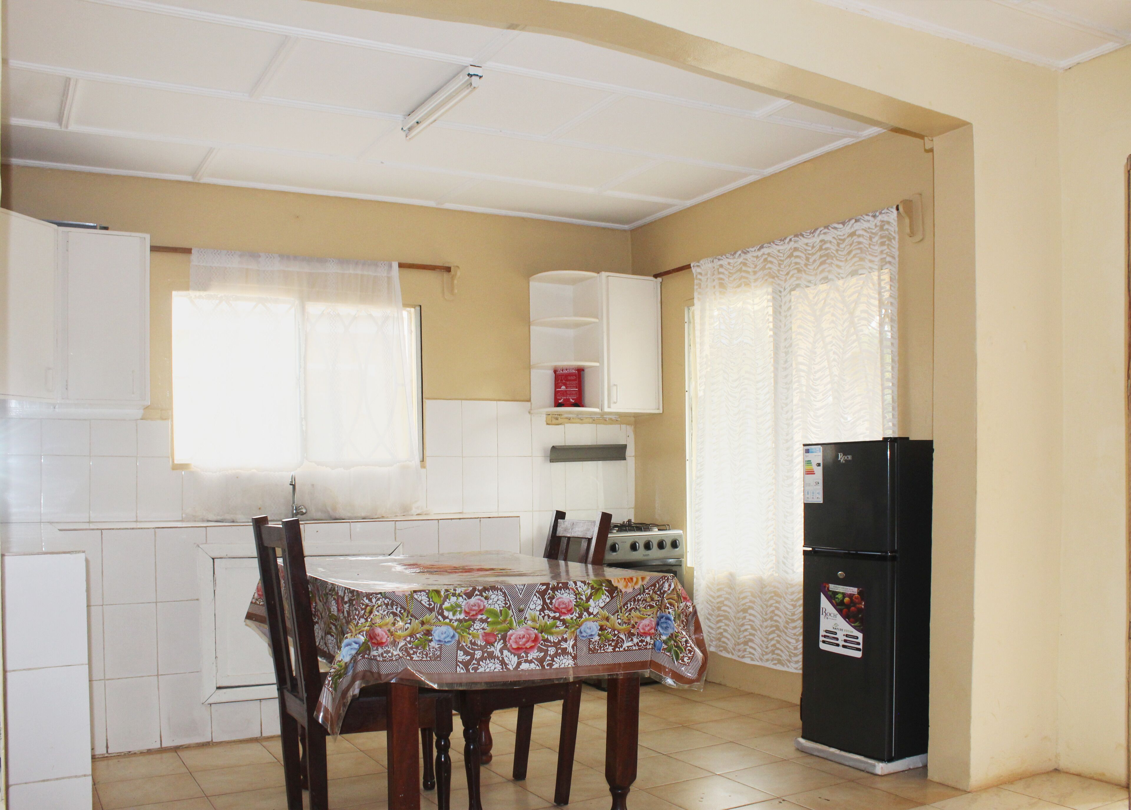Una cocina compacta con armarios blancos, una mesa de comedor con mantel floral, una estufa y un refrigerador negro.