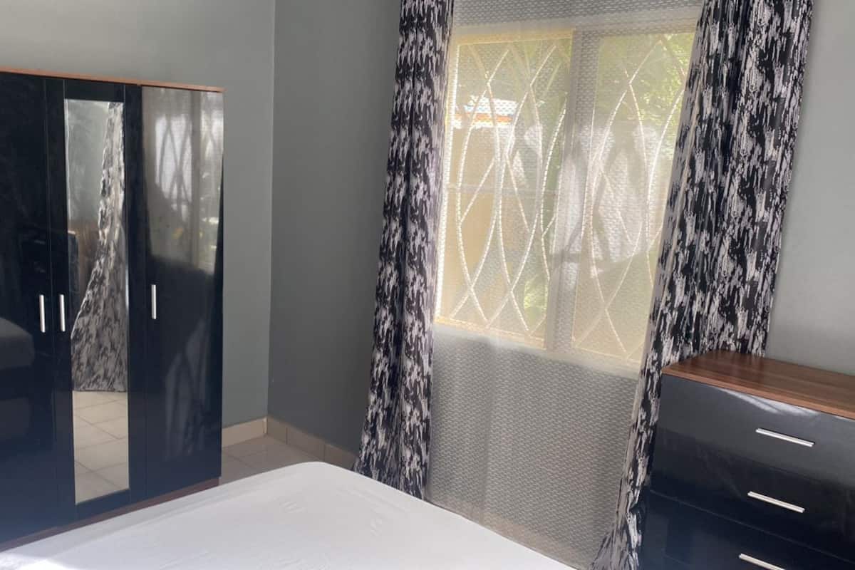 Un dormitorio con cama, armario, ventana con cortinas y escritorio.