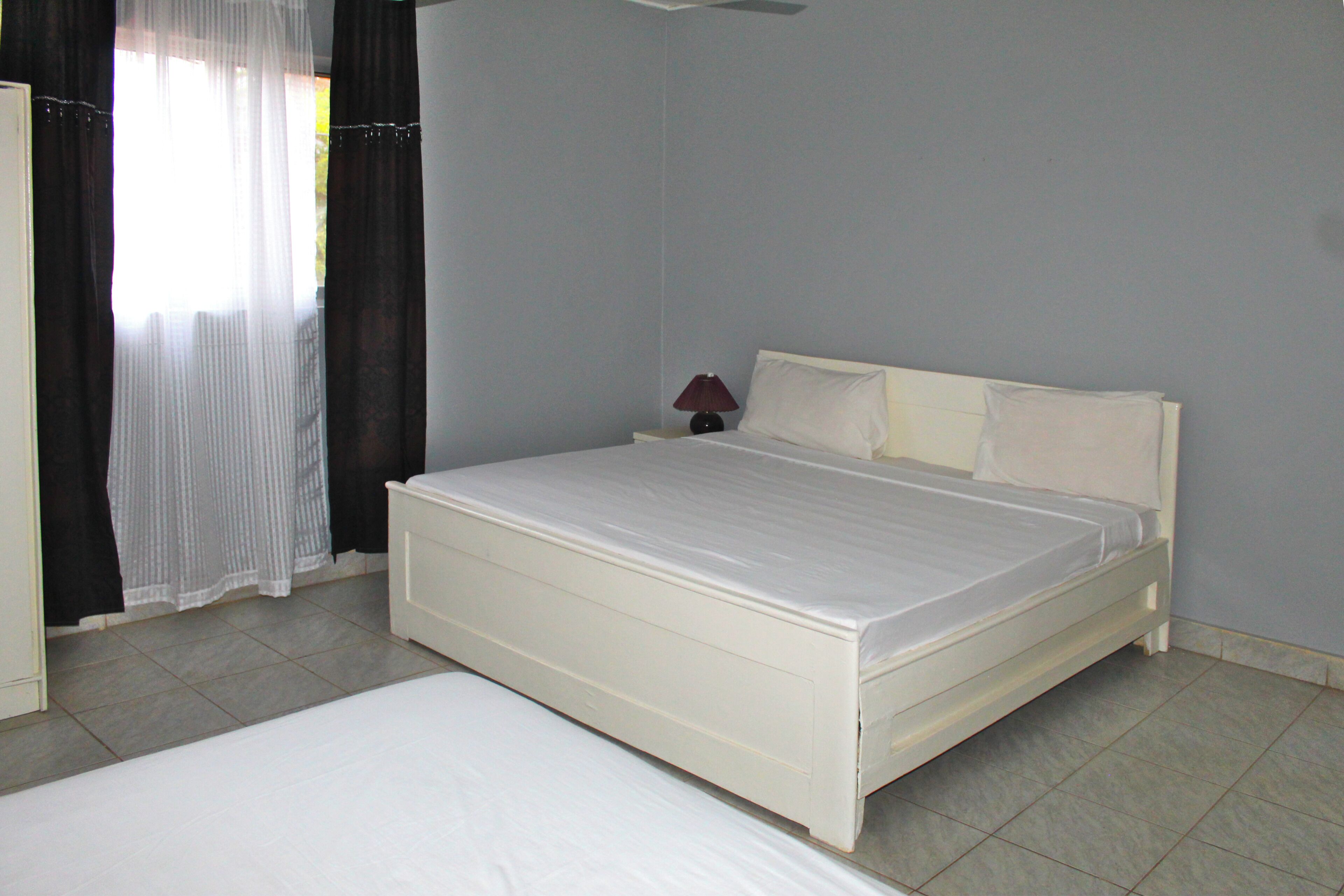 Un dormitorio con una cama individual, una mesita de noche, una lámpara y una ventana con cortinas.