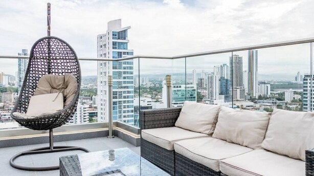A balcony with a wicker chair and a sofa, offering a city view.