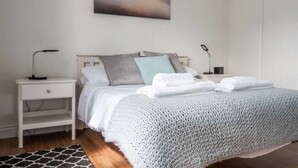 A neatly made bed with a grey knitted blanket, a bedside table with a lamp, and a nightstand with a lamp. - Vectis Holiday Homes, Modern, spacious apartment, great location, EV Charging (Shanklin)