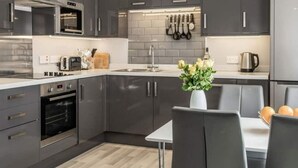 A modern kitchen with grey cabinets, a built-in oven, a microwave, and a dining area with a table and chairs. - Vectis Holiday Homes, Modern, spacious apartment, great location, EV Charging (Shanklin)