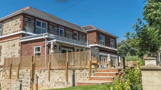 A two-story house with a stone facade, a balcony, and a well-maintained lawn. - Vectis Holiday Homes, Modern, spacious apartment, great location, EV Charging (Shanklin)