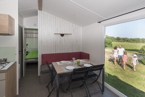 Uma sala de jantar com uma mesa posta para quatro pessoas, um banco e vista para uma família caminhando lá fora.