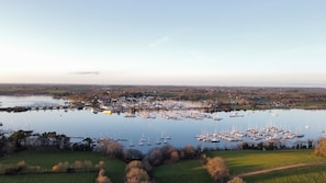 Uma marina com vários barcos atracados, cercada por campos verdes e uma cidade ao longe.