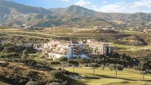 A large, multi-story building with a Mediterranean architectural style, surrounded by lush green hills and a golf course. - Guest favorite! Family apartment, terrace, spectacular views & pool near sea (Mijas costa)
