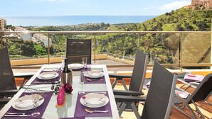 A dining table set for two with a view of a coastal landscape. - Guest favorite! Family apartment, terrace, spectacular views & pool near sea (Mijas costa)