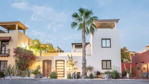 Un edificio moderno de varios pisos con techo plano, ventanas amplias y un jardín bien cuidado con cactus y palmeras.