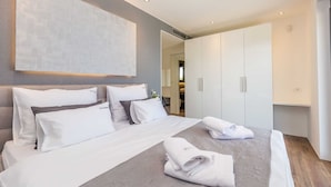A modern hotel room with a large bed, white linens, a grey patterned bedspread, and a large abstract painting on the wall. - Villa QUADRA with heated pool (Pinezići)