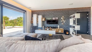A modern living room with a large window, a flat-screen TV, a sofa, and a coffee table. - Villa QUADRA with heated pool (Pinezići)