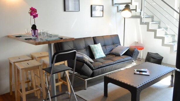 A modern living room with a sofa, chairs, a coffee table, and a small dining area with stools. - Quiet 2 bedrooms apartment (Biarritz)