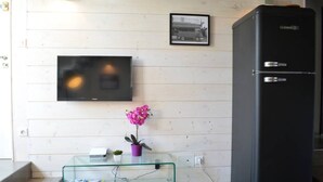 A compact kitchen with a black refrigerator, a glass coffee table with a potted orchid, and a flat-screen TV mounted on the wall. - Quiet 2 bedrooms apartment (Biarritz)