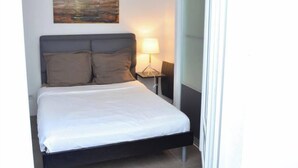 A neatly made bed with a white sheet and two pillows, a bedside lamp, and a painting on the wall. - Quiet 2 bedrooms apartment (Biarritz)
