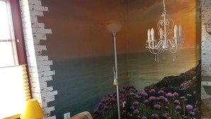 A living room with a sofa, a lamp, a chandelier, and a mural of a sunset over the ocean.