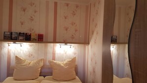 A bedroom with striped wallpaper, a bed with white bedding, and a shelf with books.