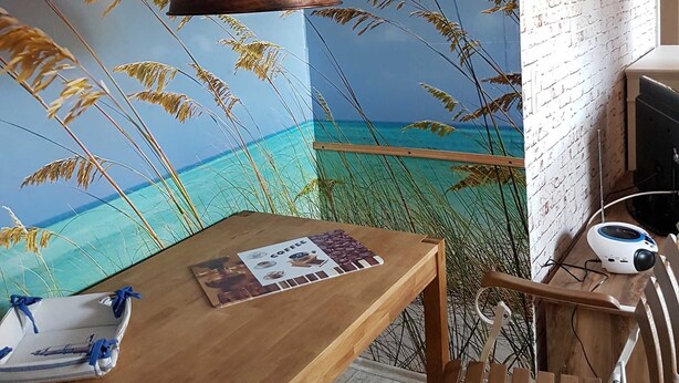 A dining area with a wooden table, chairs, a pendant light, and a mural of a beach scene.
