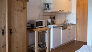 A compact kitchen with white cabinets, a wooden table, and a microwave. - Romantic studio with garden, SWIMMING POOL, mountain railways for free (Telfes)