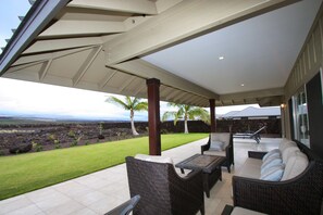 Un patio cubierto con mobiliario de mimbre, vistas a un jardín ajardinado y un muro de piedra.