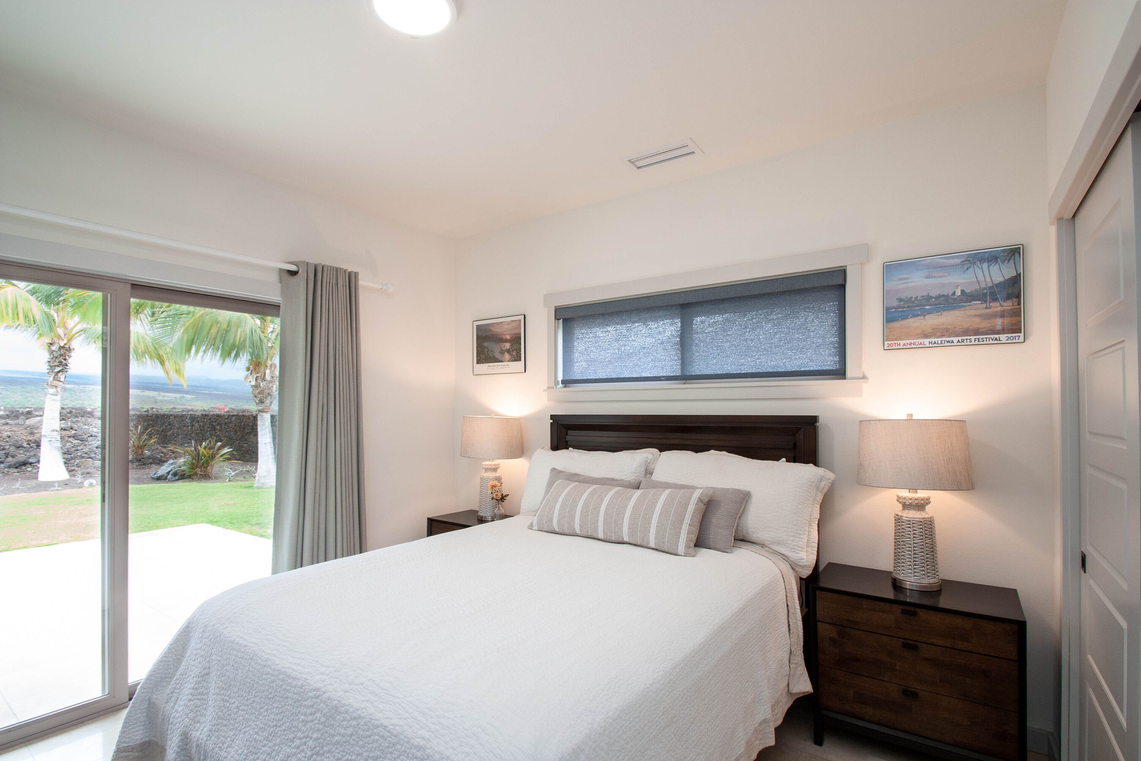 A bedroom with a large bed, two bedside tables with lamps, a window with a view of the outdoors, and a framed picture on the wall.