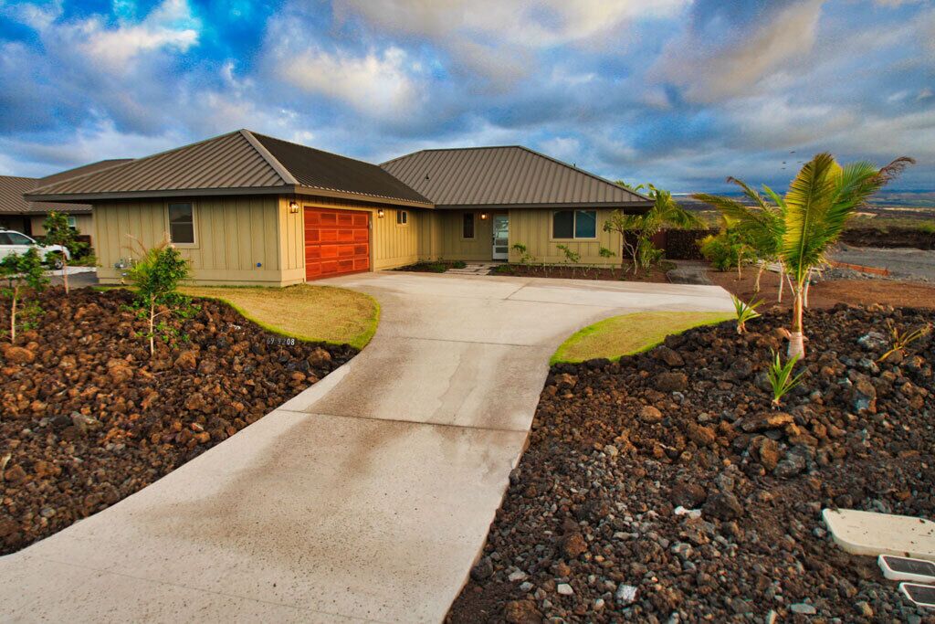 A single-story house with a red garage door, a driveway, and a small garden with palm trees.