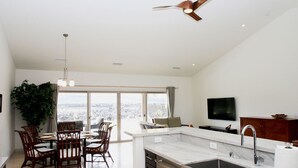 A modern kitchen with a large island, a dining area with chairs, a ceiling fan, and a TV mounted on the wall. - Family Friendly Home with Mountain Views, Private Lanai, and Beach Accessories (Waikoloa Village)