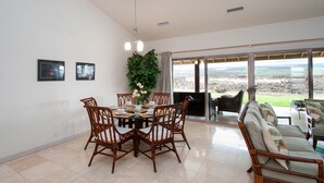A dining area with a round table and chairs, a potted plant, and a view through large glass doors. - Family Friendly Home with Mountain Views, Private Lanai, and Beach Accessories (Waikoloa Village)