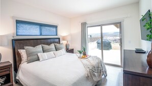 A bedroom with a bed, a nightstand, a lamp, a window with a view, and a sliding door to a balcony. - Family Friendly Home with Mountain Views, Private Lanai, and Beach Accessories (Waikoloa Village)
