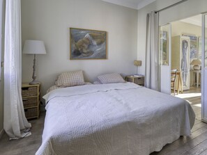 Een slaapkamer met een groot bed, een schilderij aan de muur en uitzicht op een andere kamer door een geopende deur.