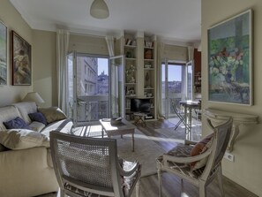 Een ruime woonkamer met een bank, een stoel, een televisie en een balkon met uitzicht op de stad.