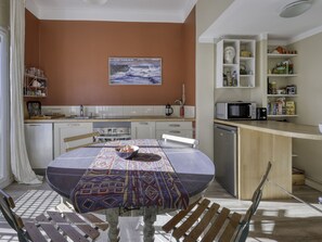 Een moderne keuken met witte kastjes, een eettafel met een tafelkleed met dessin, en een schilderij aan de muur.