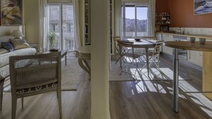 Un vaste espace de vie comprenant un canapé, une table à manger et des chaises, un balcon avec des rideaux, ainsi qu’un coin cuisine offrant une vue sur la ville.