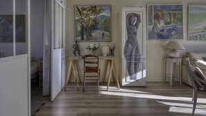 Une pièce avec un plancher en bois, un bureau avec une chaise et une lampe. Il y a des tableaux au mur et une statue sur le bureau.